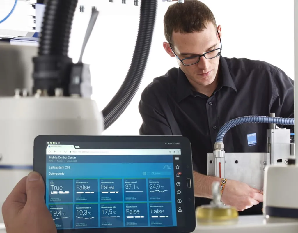 Tablet running the control Mobile Control Center with live process data from a plant control system, a technician working on the machine behind it.