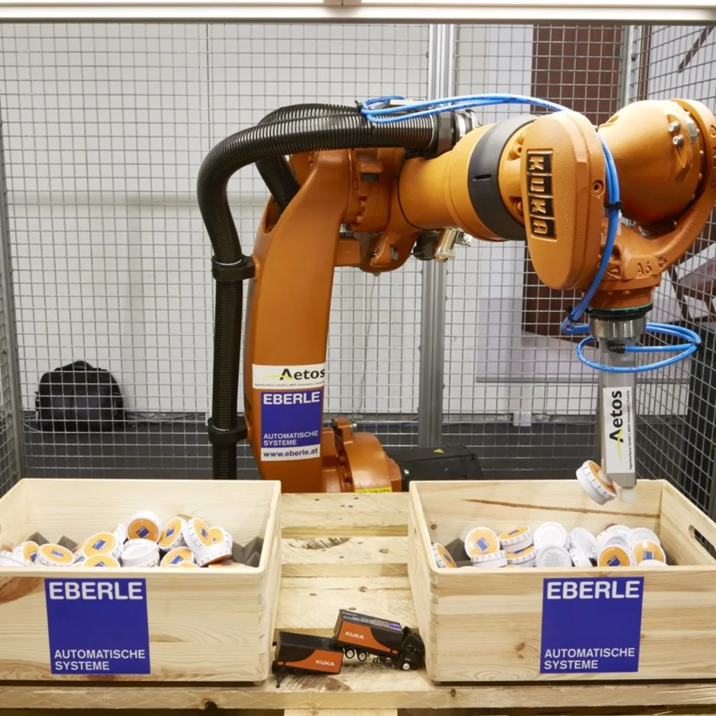KUKA industrial robot with a suction gripper picking parts from a wooden crate in a robot cell